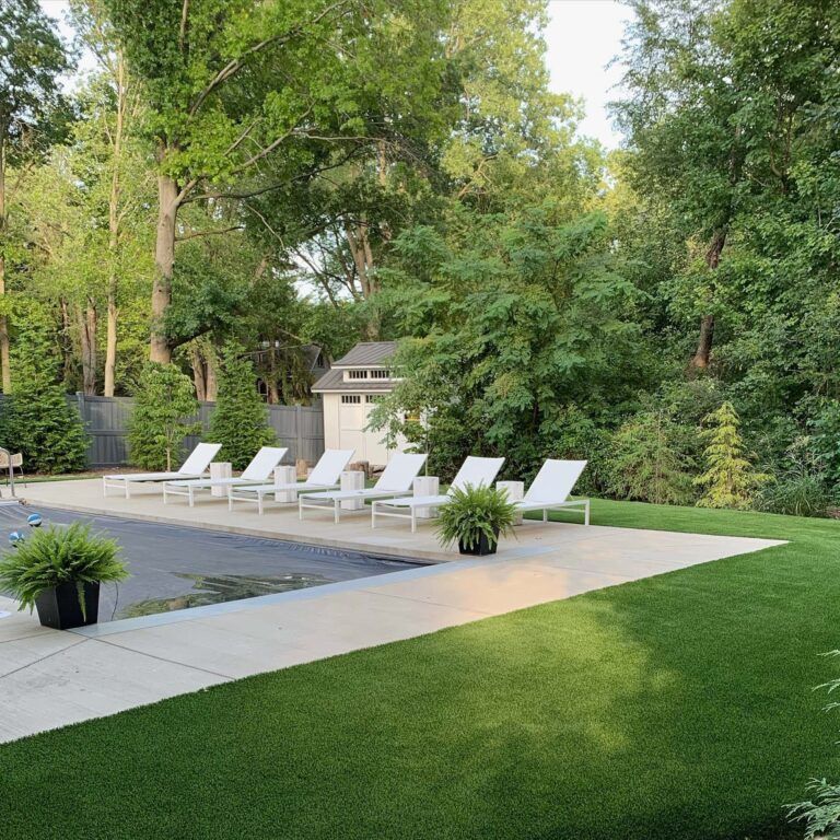 Poolside scene with white lounge chairs, green lawn, trees, and small shed.