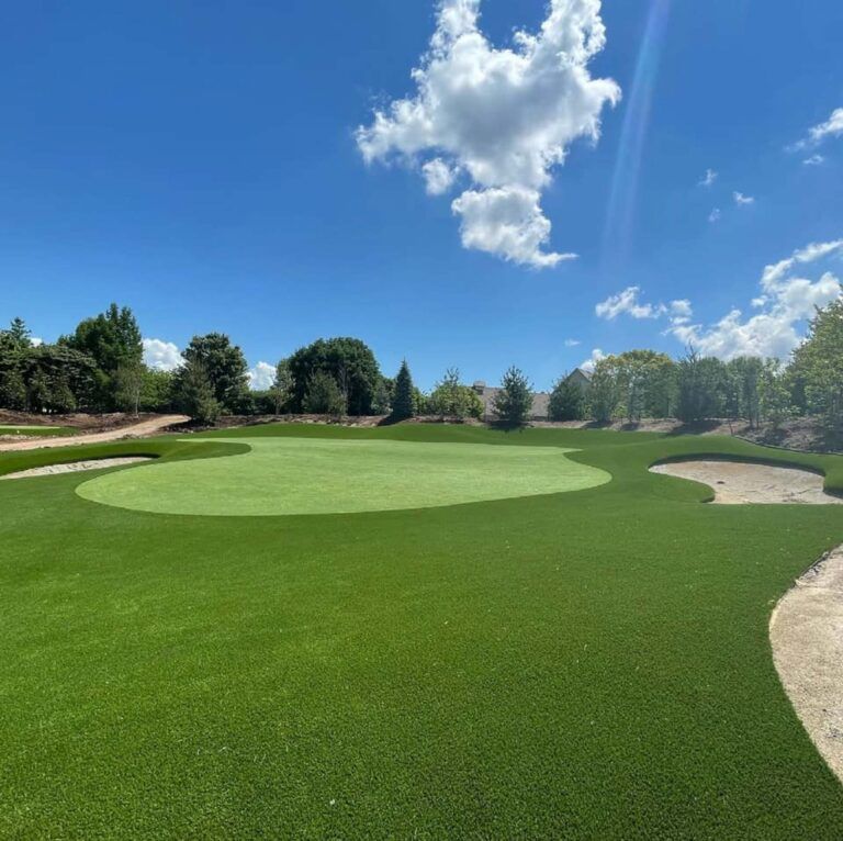 Green golf course with sand traps under a blue sky with fluffy white clouds.