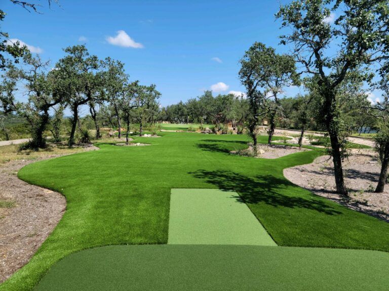 Green artificial turf golf course with trees under a blue sky.