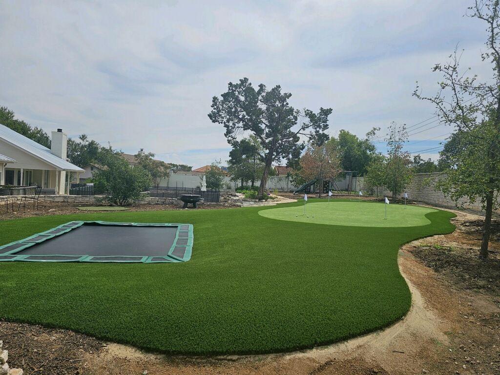 Backyard with artificial turf, a trampoline, and a putting green under a cloudy sky.