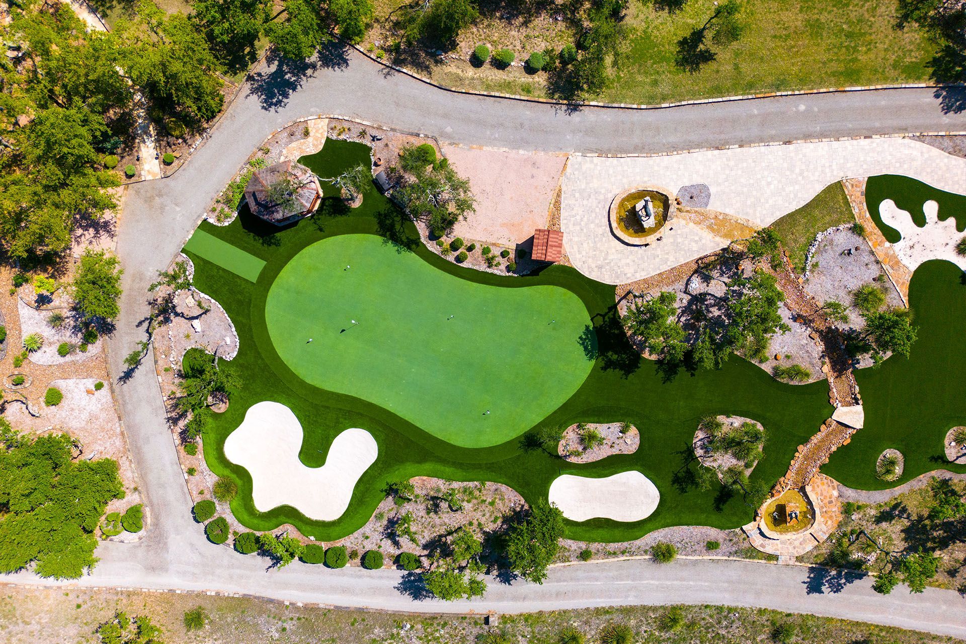 Aerial view of a custom putting green with sand traps, rock formations, and a water feature.