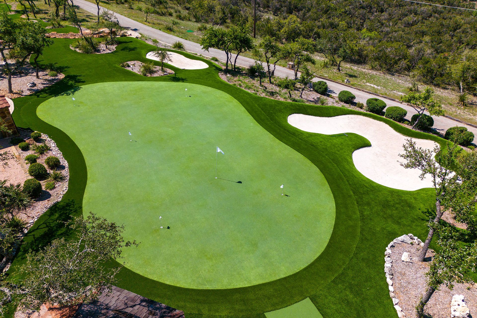 Aerial view of a private putting green with sand traps, surrounded by trees and shrubs.