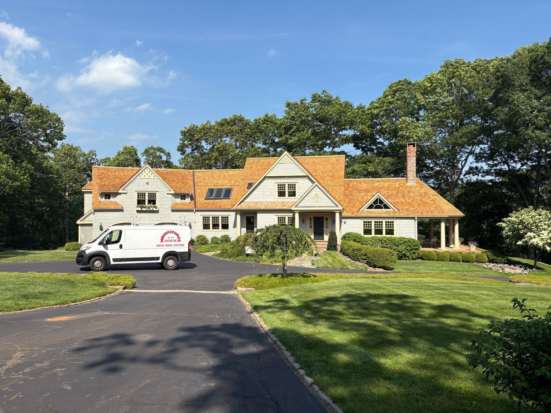 Large cream-colored house with orange roof, white van in driveway, and green lawn under a blue sky.