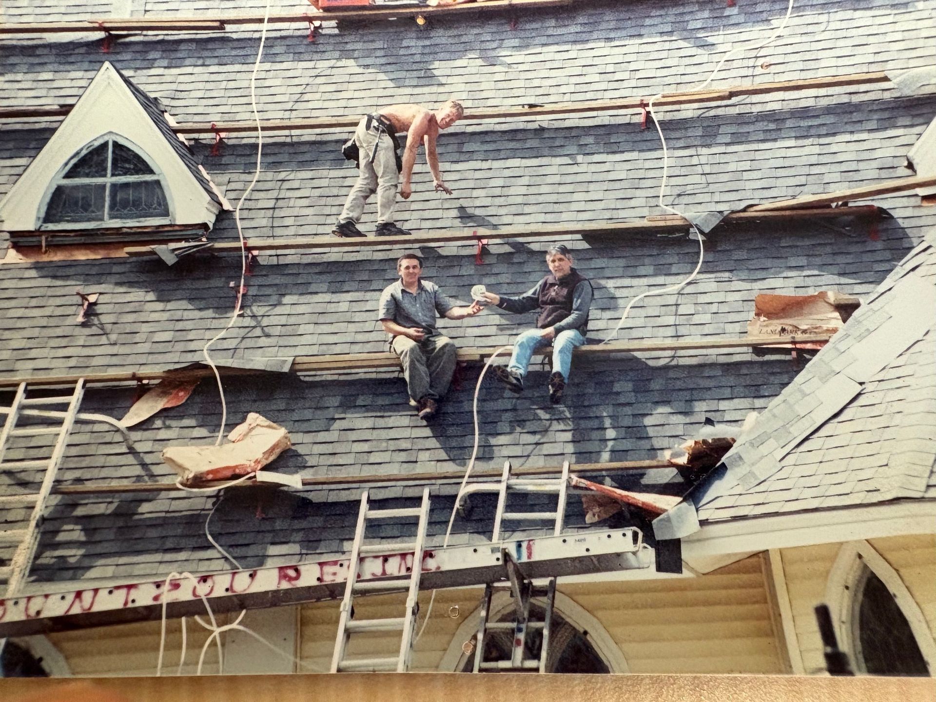Roofers take a break on a damaged roof with a triangular window.