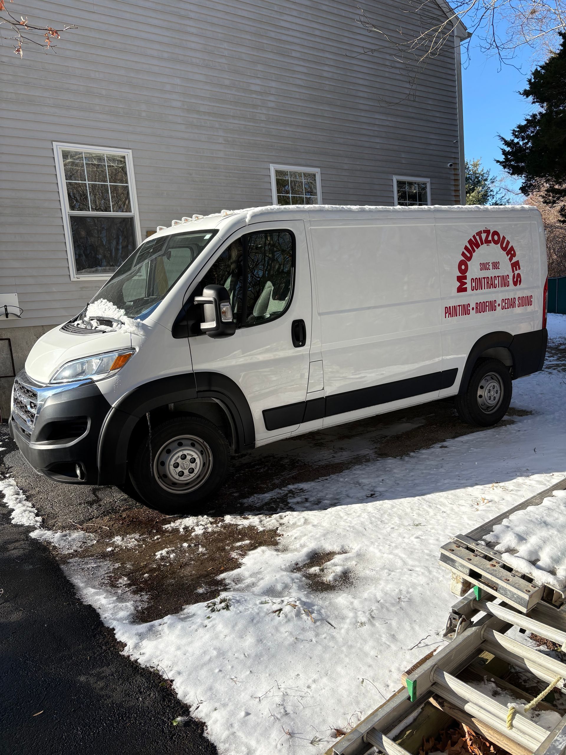 White service van parked in a snowy driveway beside a house; logo with phone number on the side.
