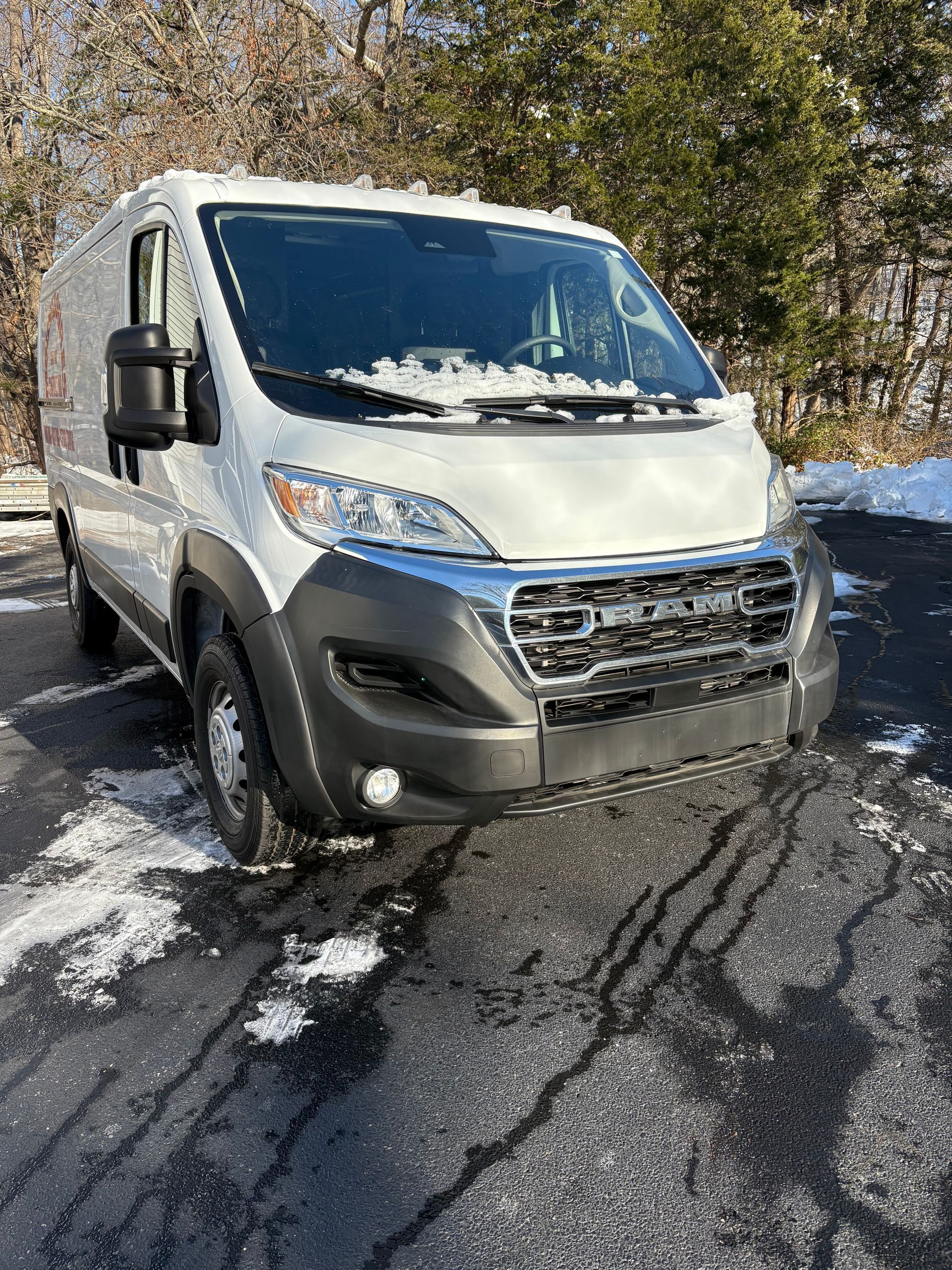 White cargo van parked on a wet asphalt surface with melting snow, partly sunny day.