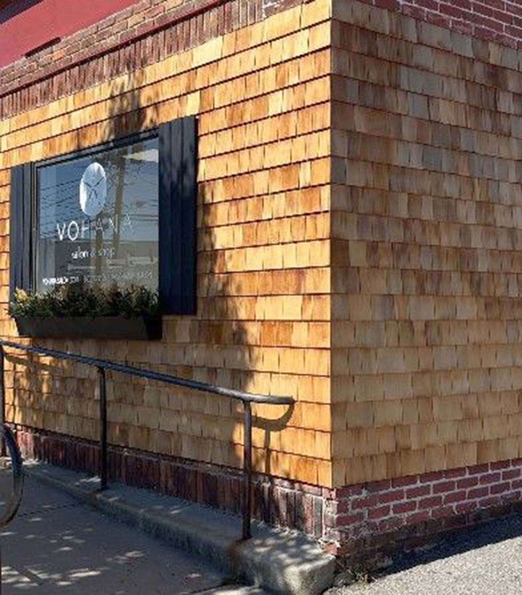 Corner building with wood shingles and a window with black shutters, ramp, and a brick base