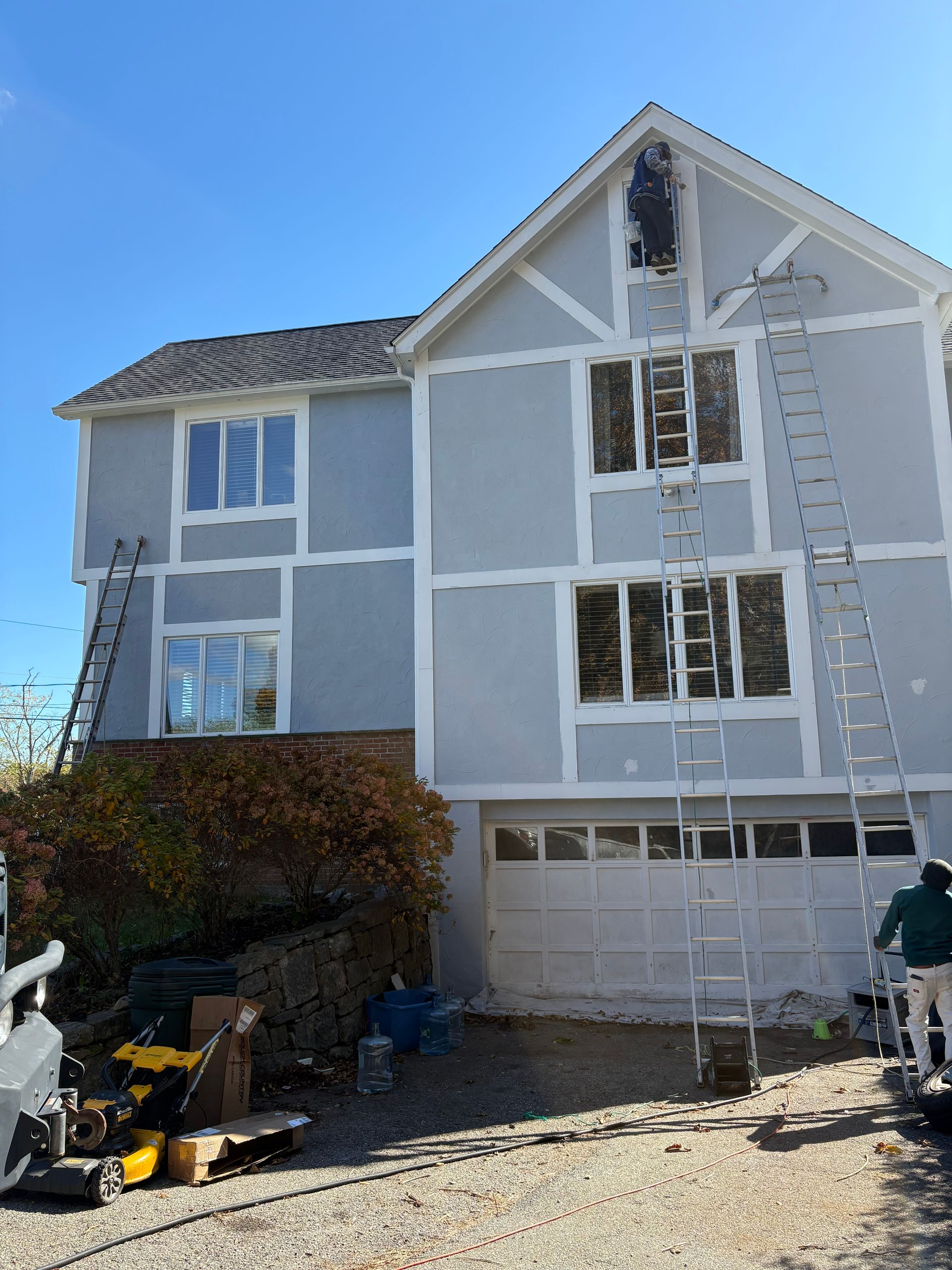 House exterior being painted, blue walls with white trim. Ladders and workers visible.