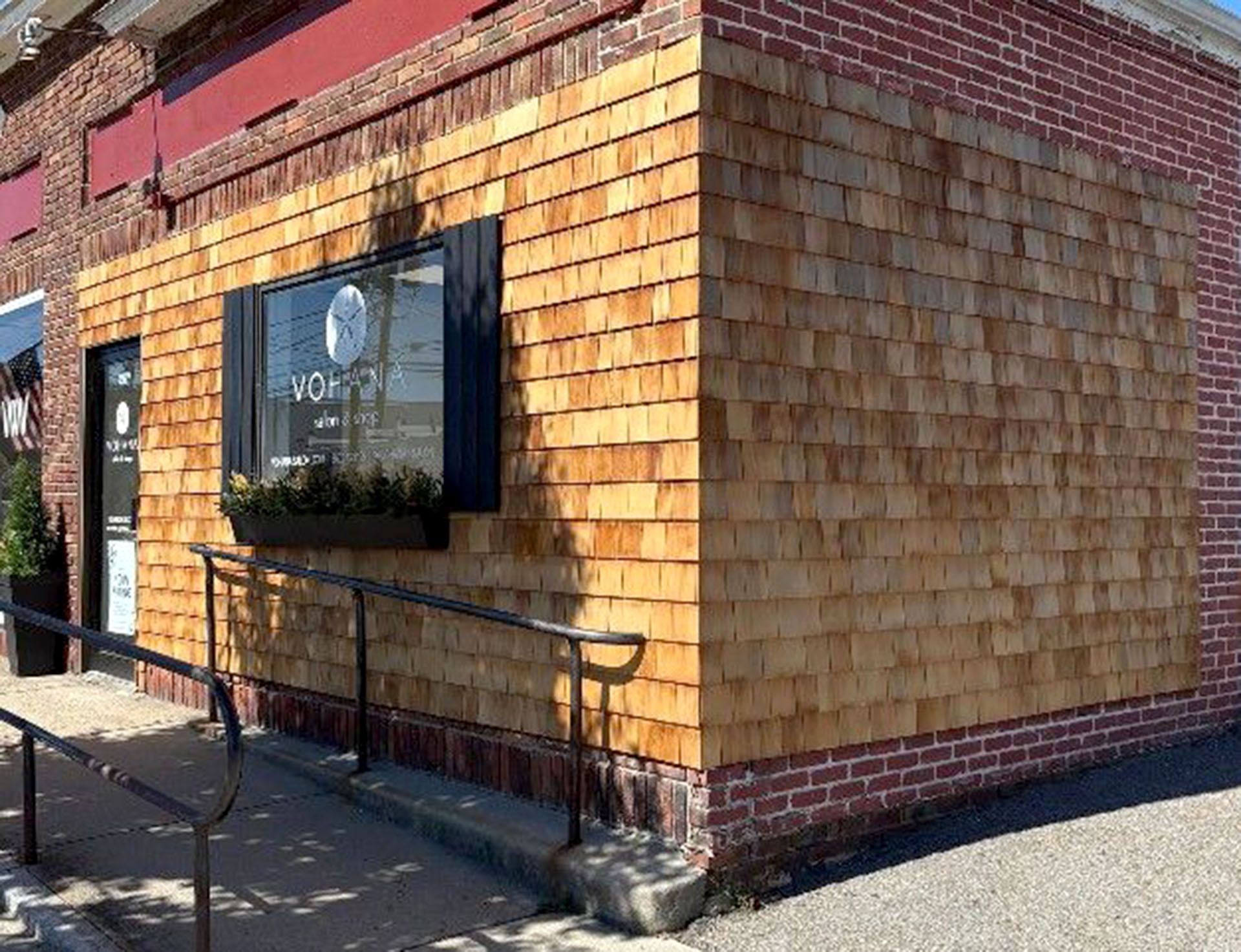 Building exterior with wood shingle siding, brick accents, window with black shutters, and accessible ramp