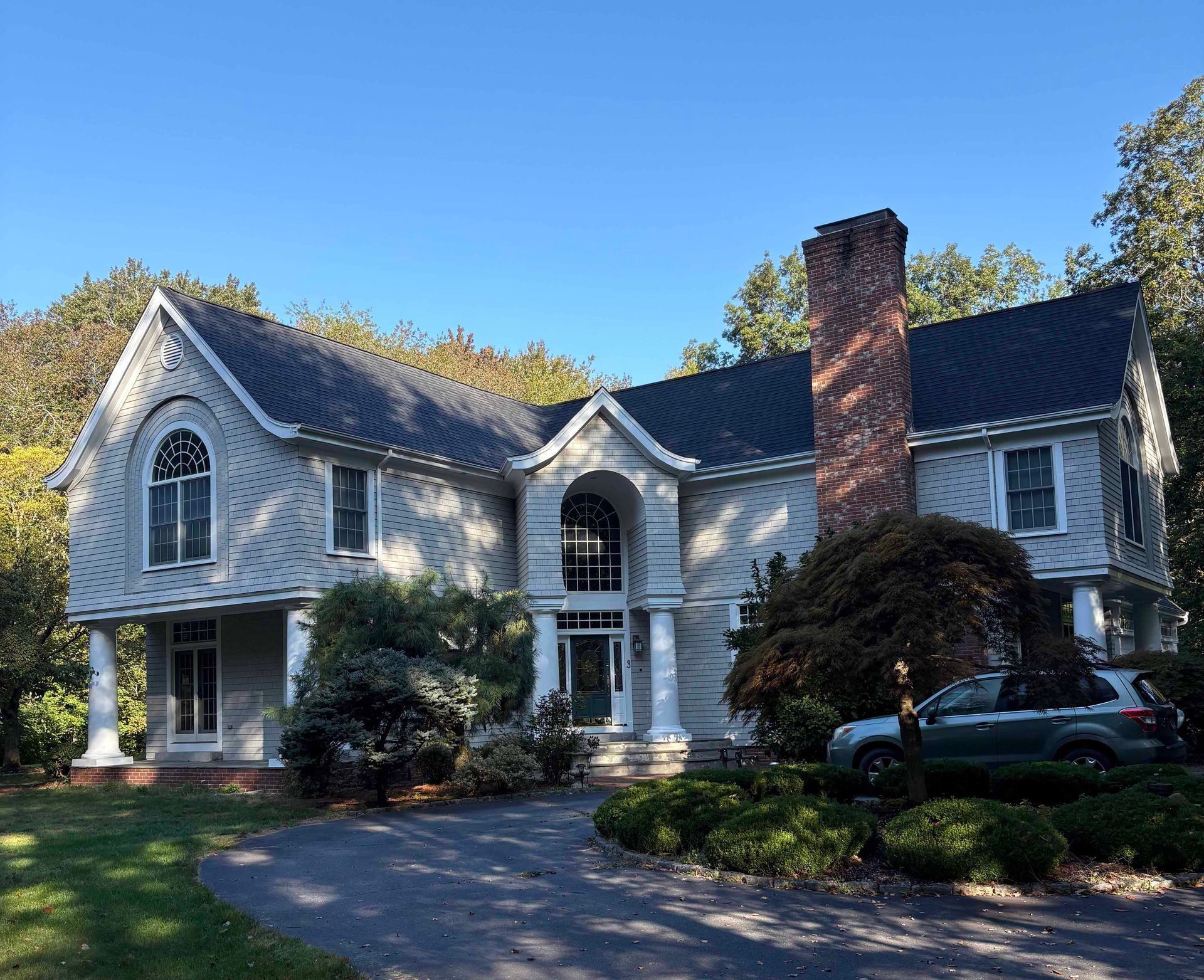 Two-story gray house with a dark roof, tall brick chimney, and a car in the driveway.