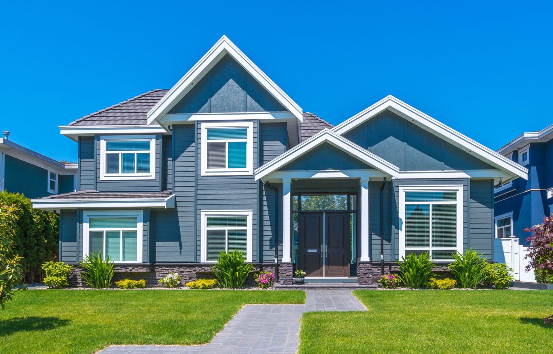 Blue house with white trim, front yard, and pathway on a sunny day.