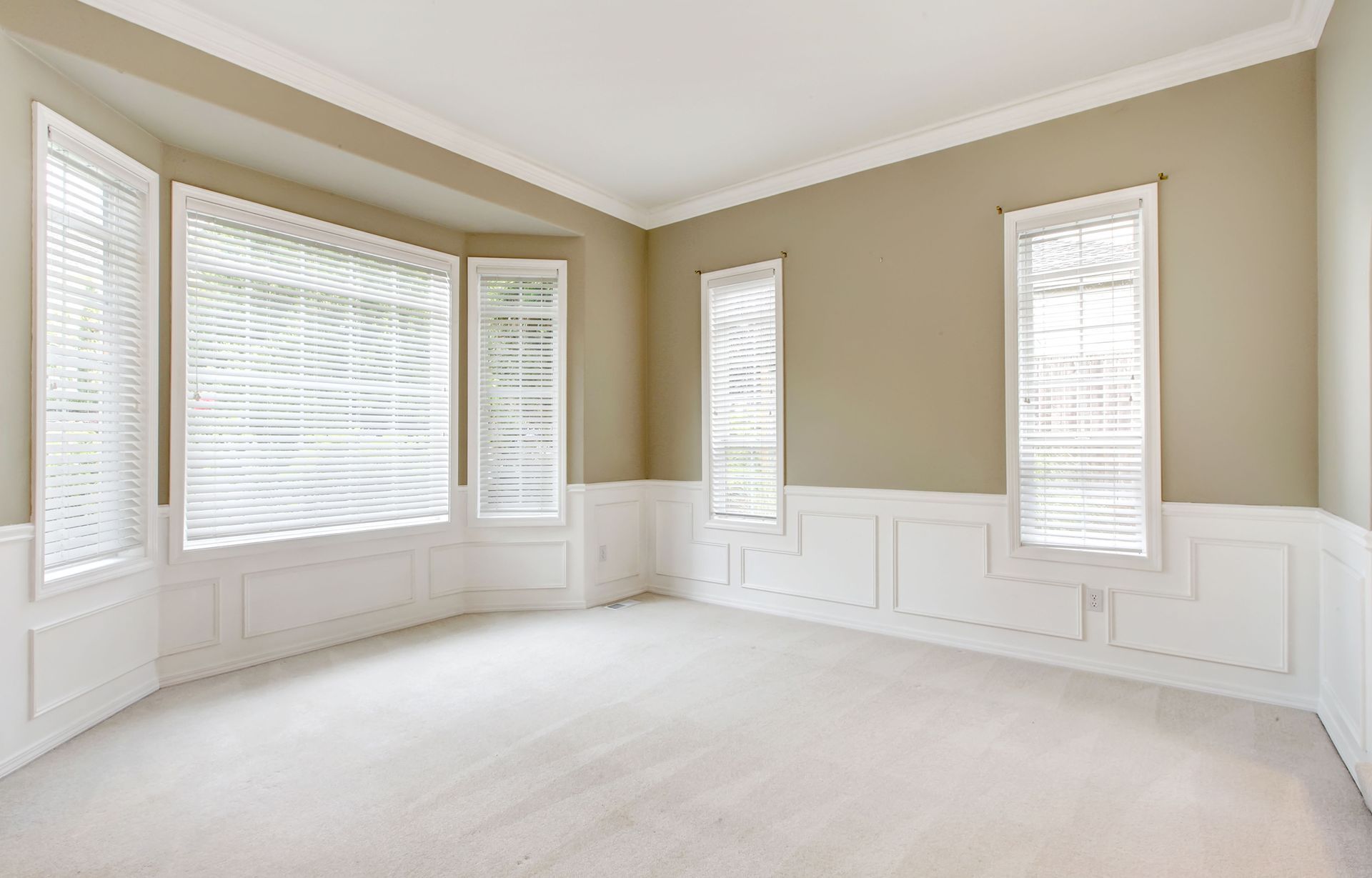 Empty room with white walls, carpet, and windows with blinds.