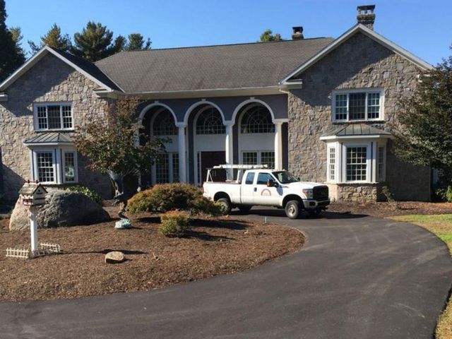 Stone house with white truck parked in front. Driveway leads to house. Blue sky.