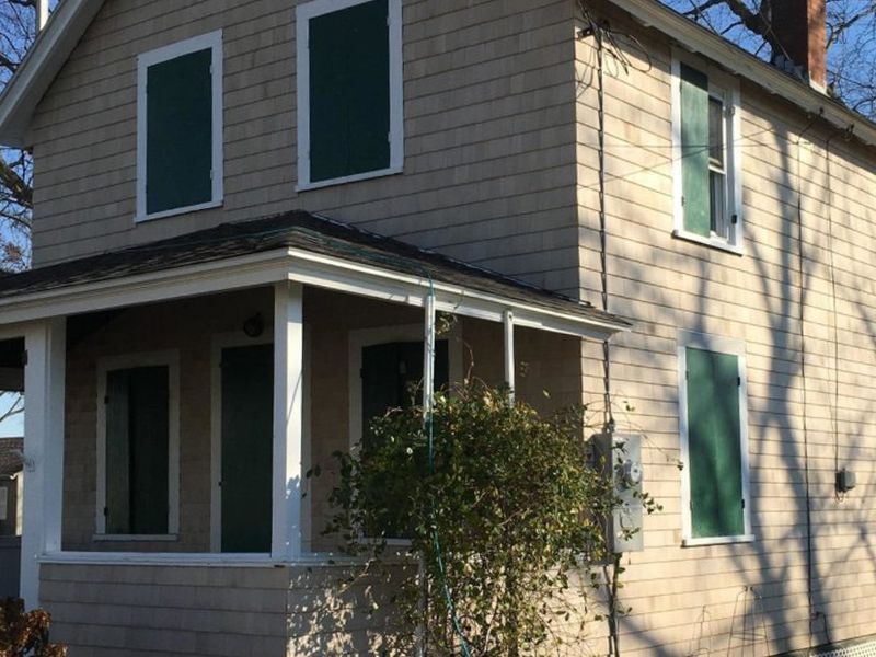 Two-story house with beige siding and green shutters. A small porch with white posts.