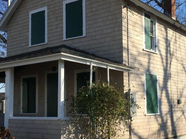 Two-story house with beige siding and green shutters. A small porch with white posts.