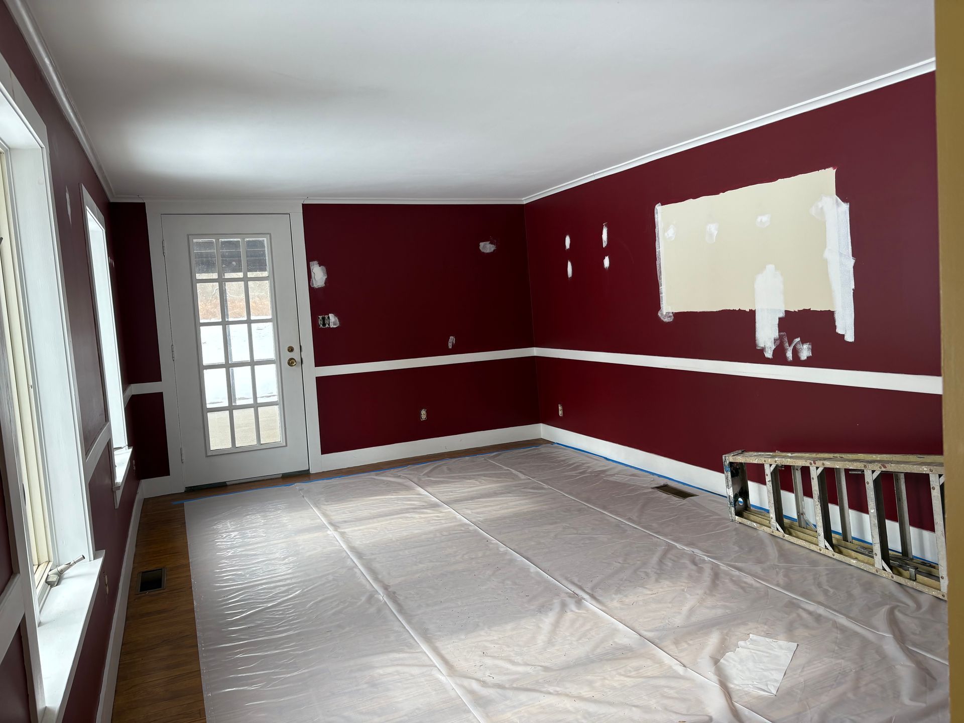 Room with burgundy walls, white trim, and plastic sheeting on the floor, possibly under renovation.