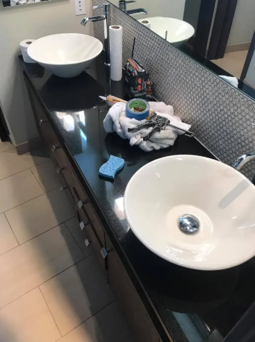 A modern double-sink vanity with white bowl sinks on a black countertop, featuring tools and materials for installation.