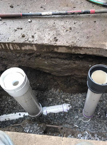 Two vertical PVC pipes with end caps, connected to a horizontal pipe buried in a trench filled with crushed stone.
