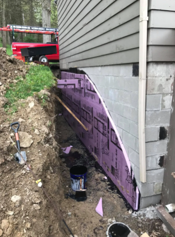 A foundation wall under repair, featuring purple foam insulation panels, a trench, and a red truck in the background.