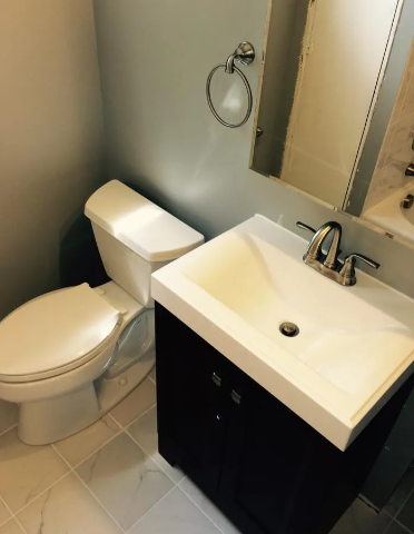 A bathroom featuring a white toilet, a dark wood vanity with a white rectangular sink, and a circular towel ring.