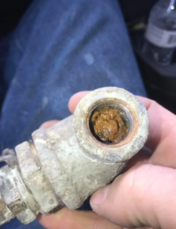 A close-up of a hand holding a threaded metal pipe fitting that is severely clogged with brown, oxidized rust buildup.
