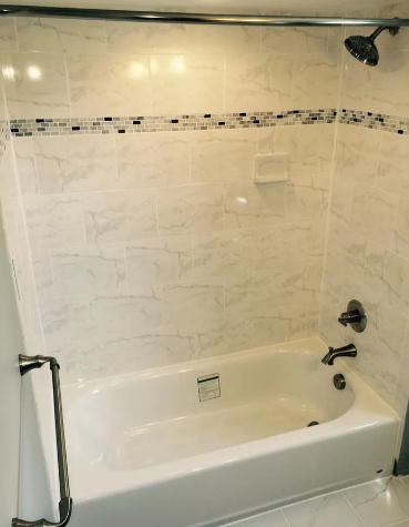 A bathtub and shower combo with marble-look wall tiles, a glass accent border, and dark metal fixtures.