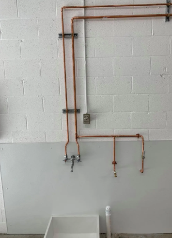 Copper pipes mounted on a white brick wall above a utility sink, featuring a faucet and two downward-facing valves.