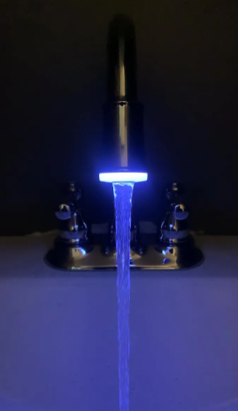 A chrome bathroom faucet in a dark room with a glowing blue LED light attachment casting light on the running water.