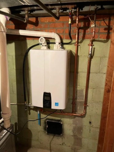 A white tankless water heater mounted on a cinder block basement wall, connected to white PVC venting and copper pipes.