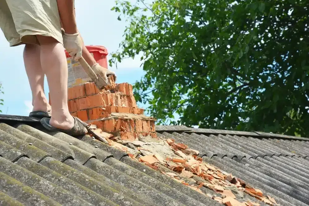 Workers removing bricks from a roof, with debris sliding down the sloped tiles