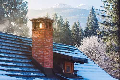 Snowy cabin roof with red brick chimney in a mountain forest landscape
