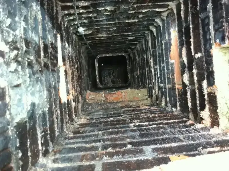 Narrow rusty metal tunnel or shaft receding into darkness, with worn, corroded walls and floor
