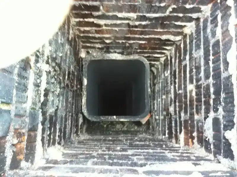 Inside a brick-lined square chimney or vent shaft, viewed looking upward into darkness