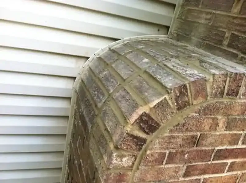 Close-up of a brick chimney beside white vinyl siding with a curved top