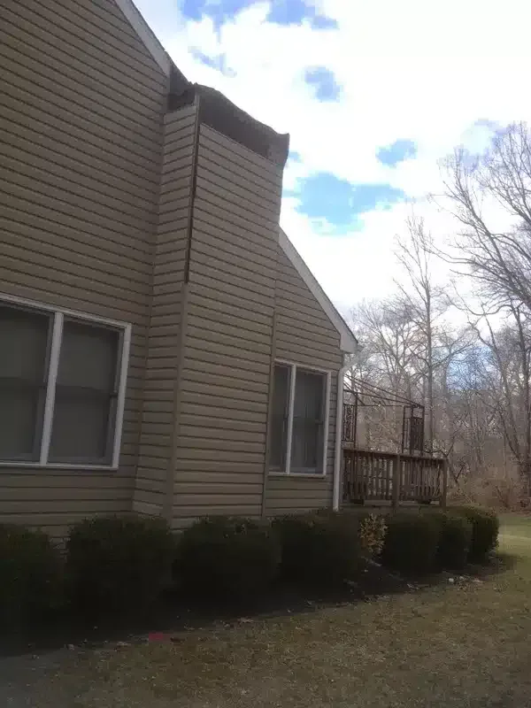 Tan house exterior with windows, shrubs, and a small deck under a cloudy sky