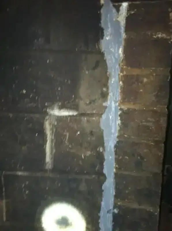 Dark brick wall with a vertical blue-painted strip and a white circular mark near the bottom.