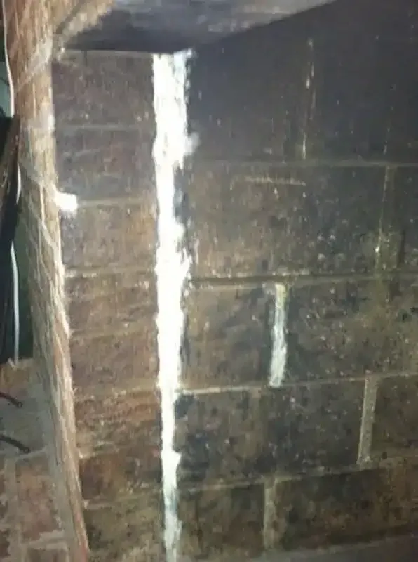 Dimly lit stone wall with a vertical crack filled with white mortar or sealant