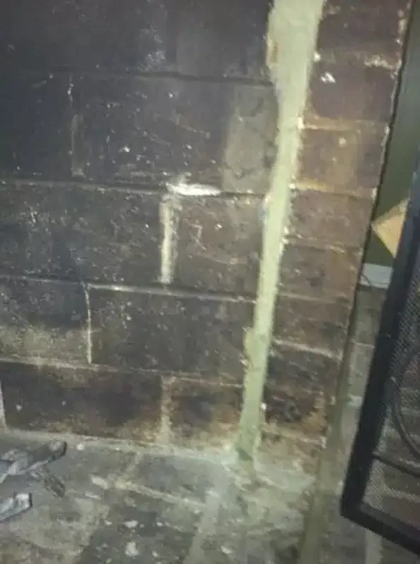 Close-up of a dark brick wall with a vertical crack sealed by pale mortar or plaster