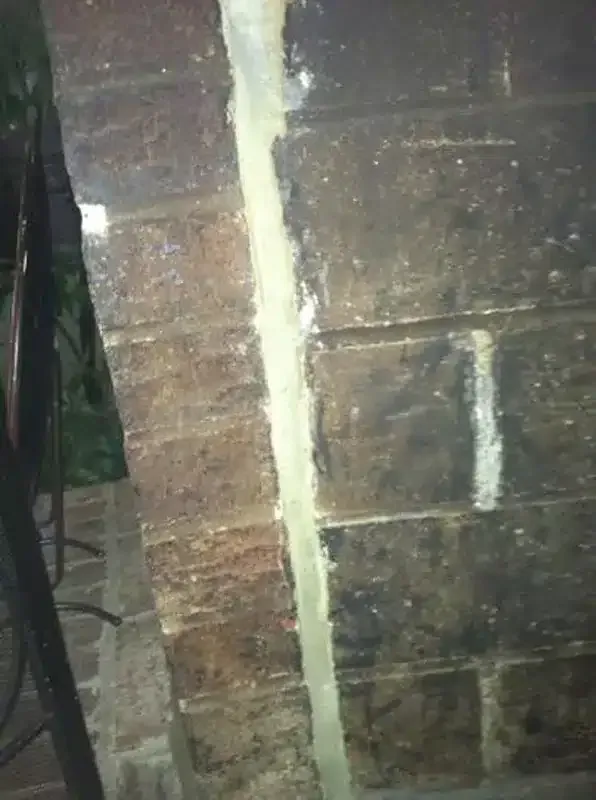 Close-up of a cracked brick wall with a vertical strip of white sealant or plaster running down the center.