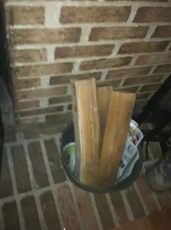 Two wooden boards standing in a bucket against a brick wall indoors