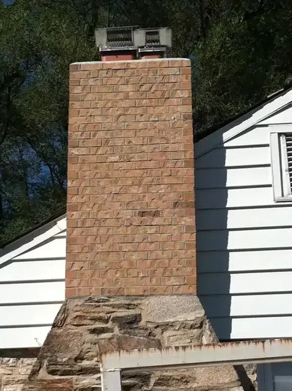 Brick chimney on a white house with a stone base and a small metal vent on top