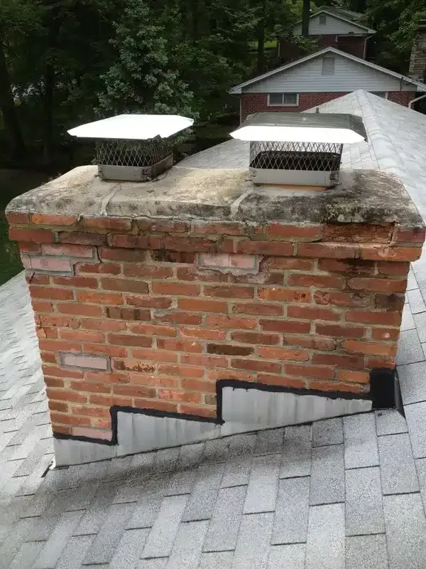 Brick rooftop chimney with two metal vents and a dark patch on the lower side