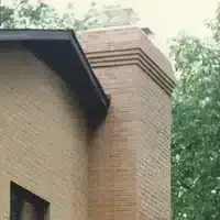 Brick house corner with a large narrow brick chimney rising above the roofline.