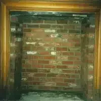 Brick fireplace with a wooden mantel, mostly blocked by a brick wall or chimney closure