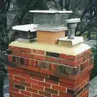 Brick chimney with a metal chimney cap and wire mesh on top in a snowy outdoor setting