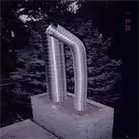 Metallic double-pipe sculpture on a concrete base outdoors, against a dark wooded background