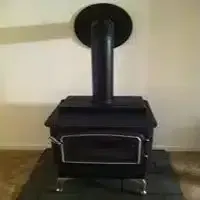 Black freestanding wood stove with chimney pipe on a tiled floor against a beige wall