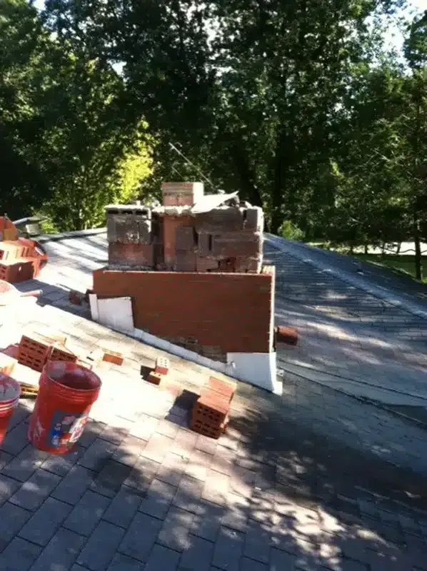 Brick chimney under construction on a sloped roof with trees in the background