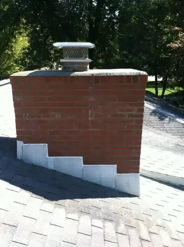 Brick chimney on a shingled roof with a metal vent cap.