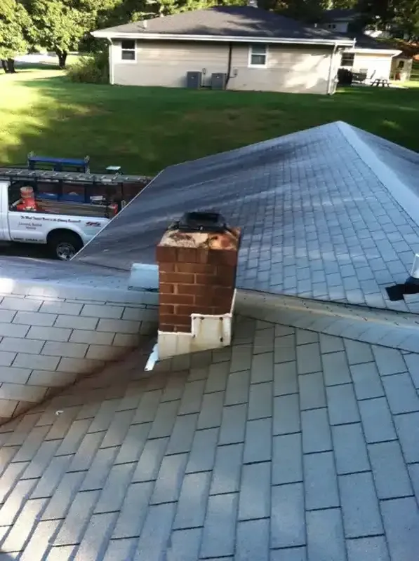 Roof with brick chimney and parked utility truck in a suburban neighborhood.